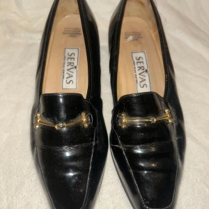Servas Lackskor, Svarta, Storlek 35 - Eleganta svarta lackskor från Servas. Klassisk modell med en dekorativ guldfärgad detalj över foten. Perfekt för både vardag och fest.
