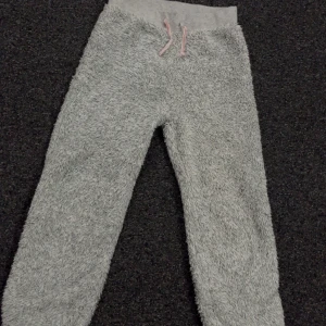 Grå fluffiga mjukisbyxor H&M 134/140 - Supermysiga grå mjukisbyxor från H&M i storlek 134/140. Byxorna är fluffiga och har en bred resår i midjan med rosa snörning. Perfekta för chill dagar hemma eller när du vill vara extra bekväm.