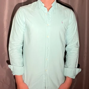 Ljusblå skjorta från Ralph Lauren - Sommaren här!☀️Säljer därför en snygg ljusblå skjorta från Ralph Lauren med klassisk button-down krage och broderad logga på bröstet. Skjortan har långa ärmar och stängs med knappar framtill. Perfekt för dig som gillar stilrena och fräscha plagg nu inför sommaren🤗