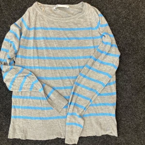 Gråblå randig tröja från Zara - Säljer en tunn, stickad tröja från Zara i grått med blåa ränder. Tröjan har rund halsringning och långa ärmar. Perfekt för lager-på-lager och chill vardagsstil.