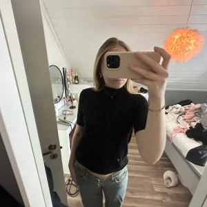 Svart topp med kort ärm - Säljer en svart topp med korta ärmar och hög hals. Toppen har en slim passform som sitter snyggt på kroppen. Perfekt för dig som vill ha något stilrent men ändå med lite extra shine.