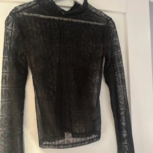 Svart meshtopp - En svart långärmad topp i mesh med printade N över hela. Printer är i ett annat material, lite sammetsaktigt. 