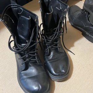 Svarta boots från NLY med snörning - Svarta boots från NLY med klassisk snörning och rund tå. Skorna är tillverkade i syntetmaterial och har en platt sula. Perfekta för dig som gillar en stilren och edgy look till höst och vinter.
