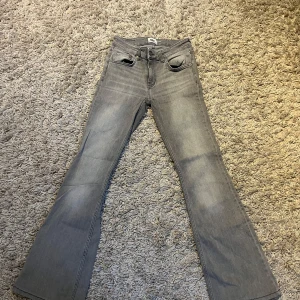 Grå bootcut jeans med låg midja - Snygga grå jeans med bootcut-modell och låg midja. Klassisk femficksdesign, dragkedja och knapp framtill. Jeansen har en ljusgrå tvätt och är tillverkade i mjukt denimtyg som ger en skön känsla. Perfekta för dig som gillar en retroinspirerad look.