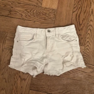 Vita jeansshorts från Zara Girls - Snygga vita jeansshorts från Zara Girls med slitna detaljer och råa kanter. Klassisk femficksmodell med knapp och dragkedja framtill. Perfekta för sommaren och ger en cool, avslappnad vibe.