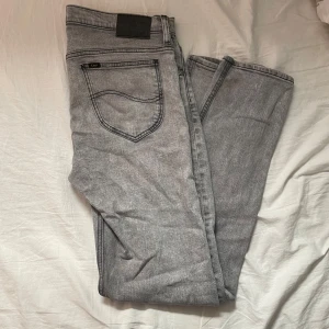 Grå jeans från Lee slim fit - Säljer ett par grå jeans från Lee med klassisk femficksdesign och svarta detaljer på bakfickorna. Storlek 33/34 (passar 32/34 också), sitter bra på mig som är 193cm 77kg. 