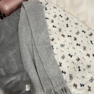 Ljusgrå mjuk halsduk med fransar - En stilren ljusgrå halsduk med fransar i ändarna. Halsduken är mjuk och fluffig, perfekt att svepa runt halsen för extra värme. Passar dig som gillar enkel och clean stil.