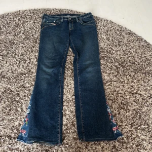 Diesel bootcut jeans med broderi - Mörkblå bootcut jeans från Diesel med snyggt broderade blommor i rött, vitt och grönt längs bensluten. Sytt själv! Storlek 30, kan diskutera pris vid snabb affär 