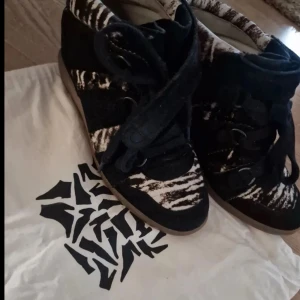 Isabel Marant sneakers med zebramönster - Unika Isabel Marant sneakers i svart och vitt zebramönster. Skorna har snörning, kardborreband och platt sula. Tillverkade i mocka och textil med coola detaljer som ger en edgy vibe. Perfekta för dig som vill sticka ut med din stil.