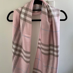 Rutig rosa sjal från Burberry - Lyxig halsduk i 100% kashmir från Burberry med klassiskt rutigt mönster i ljusrosa, beige, vitt och ljusblått. Mjuk och tunn med fransar i kanterna, perfekt att slänga över axlarna för en snygg och stilren look.