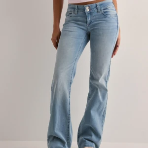 Nelly lågmidjade Ljusblå bootcut jeans med dubbla knappar - Snygga ljusblå bootcut jeans med låg midja och dubbla silverfärgade knappar i midjan. Jeansen har klassiska fickor fram och bak, samt bälteshällor. Materialet är mjukt denim i bomullsmix, perfekt för en avslappnad look.