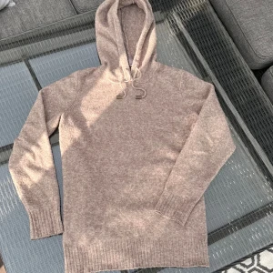 Beige stickad hoodie  - Mysig beige stickad hoodie med huva och snörning. Tröjan har långa ärmar och breda ribbade muddar vid ärmslut och nederkant. Perfekt för lager-på-lager och chill dagar. Passar dig som gillar en enkel och stilren look. Priset är ej hugget i sten.