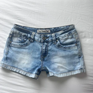 Lågmidjade jeansshorts - Snygga ljusblå jeansshorts med klassisk femficksdesign, slitna detaljer och dekorativa sömmar på bakfickorna. Shortsen har låg midja, bälteshällor och knappstängning framtill. Perfekta för varma dagar och enkel att matcha med allt. Ingen lapp men skulle säga S💕