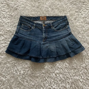 Mörkblå volang jeanskjol - Lågmidjad jeanskjol omsydd från ett par jeans. Midjemått tvärsöver - 39cm Längd - 33cm