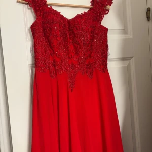 Röd långklänning med spets  - Röd långklänning från JJ’s House med vackert spet och paljettdetaljer. Perfekt för bal eller fest. Endast använd en gång. 