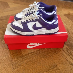 Nike Dunk Low vit/lila sneakers - Nike Dunk Low sneakers i vitt och lila med klassisk swoosh på sidorna. Dem är i modellen court purple och är stilrena med färgkombinationen lila och vit. Perfekt till dig som vill köpa ett par nya skor till sommaren ☀️Nypris 1400kr mitt pris 500kr! Så passa på och spara 900kr! Dem är 100% autentiska då kvitton har sparats🔥💯priset är inte fast!