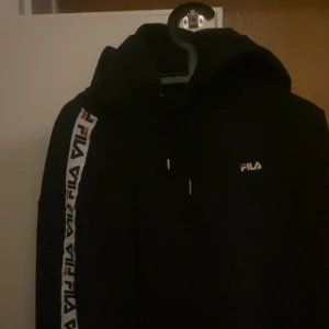 Svart hoodie från FILA med logga - Svart hoodie från FILA med klassisk logga på bröstet och längs ena ärmen. Tröjan har huva med snörning. medium men passar large