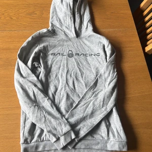 Grå Sail Racing hoodie med tryck - Snygg ljusgrå hoodie från Sail Racing med svart logotyptryck över bröstet.. Perfekt för dig som gillar en clean och sportig stil.❣️❣️ Strl 170!!