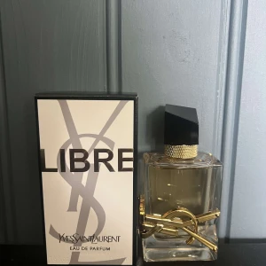 Yves Saint Laurent Libre EdP 50ml - YSL Libre Eau de Parfum i lyxig glasflaska med guldiga detaljer och svart asymmetrisk kork. Flaskan har en stilren design med YSL-logga i metall och doften är elegant och modern. Kommer med originalkartong.