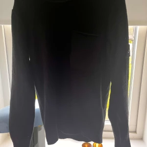 Svart stickad tröja Stone Island - Svart stickad tröja från Stone Island med klassisk patch på ärmen och en bröstficka. Tröjan har rund halsringning och långa ärmar, perfekt för dig som gillar stilren streetwear med premiumkänsla.