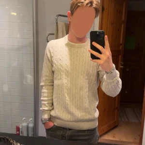 Beige kabelstickad tröja Bondelid - Snygg beige kabelstickad tröja från bondelid med rund halsringning och ribbade muddar. Perfekt för dig som gillar en klassisk och stilren look. Passar lika bra till jeans som till chinos.
