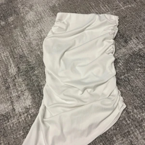 Vit omlottkjol från SHEIN XS - Snygg vit kortkjol från SHEIN i omlottmodell med draperad effekt på sidorna. Kjolen är gjord i ett ribbat syntetmaterial som ger en cool struktur och sitter tajt. Perfekt för dig som gillar trendiga och stilrena plagg.