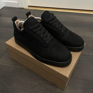 Svarta loubs från Christian Louboutin - Svarta sneakers från Christian Louboutin i mocka med klassisk röd sula och snygga svarta snören. Skorna har rund tå och platt sula, samt exklusiva detaljer som signaturlogga under sulan. Skorna har bara använt två gånger och är intill nya, lite smuts på höger sula som går bort bara man rengör de😁