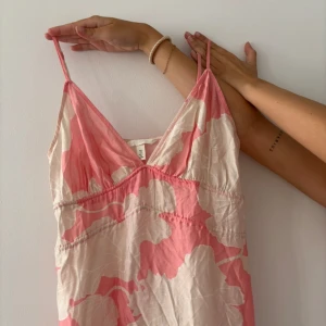 Rosa och vit blommig sommarklänning H&M - Supersöt långklänning från H&M med tunna axelband och v-ringning. Klänningen har ett stort blommigt mönster i rosa och vitt, med volang nertill!!💕💕 använd endast en gång!