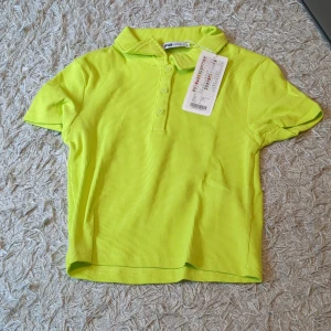 Gul/grön pikétröja - Snygg gul pikétröja med klassisk krage och tre knappar framtill. Tröjan har korta ärmar och är tillverkad i ett mjukt bomullsmaterial som känns skönt mot huden. Perfekt för dig som gillar färg och vill sticka ut lite extra.