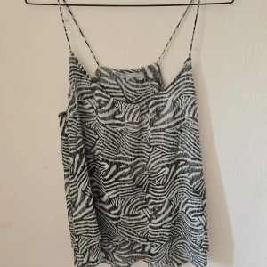 Zebramönstrad linnetopp från H&M - Snygg linnetopp från H&M med svartvitt zebramönster och tunna axelband. Toppen har en lös passform och är perfekt för dig som gillar djurmönster och vill sticka ut. Lätt och luftig känsla, passar grymt till jeans eller kjol.