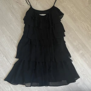 Svart volangklänning från Zara Basic - Supersnygg svart klänning från Zara Basic med tunna axelband och flera lager volanger. Lätt och luftig känsla, perfekt för dig som gillar en feminin och trendig look. Passar dig som vill sticka ut med en klassisk men ändå cool stil. Pris kan diskuteras❤️