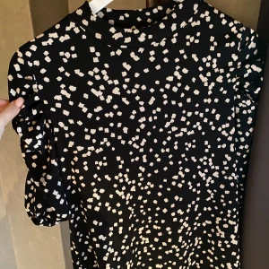 Svartvit mönstrad blus  - Snygg blus med vita prickar och puffiga kortärmar. Blusen har en rund halsringning och ett trendigt, lekfullt mönster som sticker ut. Perfekt för dig som gillar att synas och vill ha en cool look.