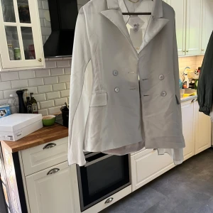Ljusgrå kostym från Max Mara i siden - Snygg ljusgrå kostym från Max Mara i glansigt sidenmaterial. Kavajen har dubbelknäppning, klassisk krage och fickor med lock. Byxorna är raka och vida med pressveck och hög midja. Perfekt för dig som vill sticka ut med en elegant och modern look.