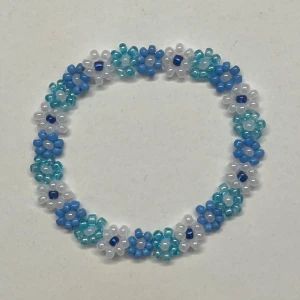 Blommigt pärlarmband i blått och vitt - Supergulligt armband med små blommor av pärlor i blått, vitt och turkost. Armbandet är elastiskt och kan göras i andra storlekar och färger💕 Superfin accessoar!