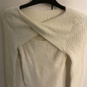 Vit stickad omlott-tröja - Supermjuk vit stickad tröja med lång ärm och snygg omlott-detalj framtill. Tröjan har en unik design med twistad front och är perfekt för dig som gillar trendiga och mysiga plagg. Passar till jeans eller kjol för en cool look.