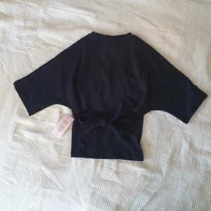 Svart Open back tee - Säljer en helt ny svart tröja från Nelly i xs! Kan även tänka mig att byta med någon som har tröjan i xxs💘 Kommer inte ändra priset