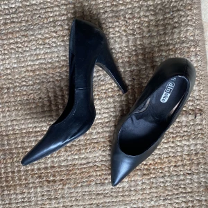 Svarta pumps med spetsig tå från DinSko - Klassiska svarta pumps från DinSko med spetsig tå och hög klack. Skorna är i slätt syntetmaterial och har en elegant, tidlös design som passar till många olika outfits. Perfekta för dig som gillar stilrena och snygga klackar.