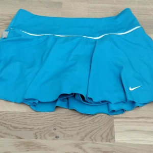 Blå Nike sportkjol  - Supersnygg blå sportkjol från Nike med inbyggda shorts och vit detalj vid midjan. Kjolen är tillverkad i Dri-FIT-material som andas och passar perfekt för tennis eller träning. 