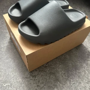 Yeezy Slides - Hej, säljer dessa jätte fina adidas Yeezy Slides i färgen Granite. Använda en gång men märks inte, helt nya. Jag säljer de då jag redan har ett par tofflor och vill bli av med dessa. Eftersom att jag vill bli av med de så kan priset diskuteras vid snabbköp, kan förekomma väldigt nedslaget pris.  Skriv gärna för fler bilder eller frågor! Boxen ingår även!