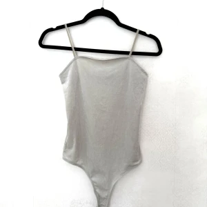 Ljusgrå body i sammet med smala band - Supersnygg ljusgrå body i mjuk sammet med smala axelband och raka kanter. Bodyn har tryckknappar i grenen för enkel på- och avtagning. Perfekt att styla med jeans eller kjol för en clean look.