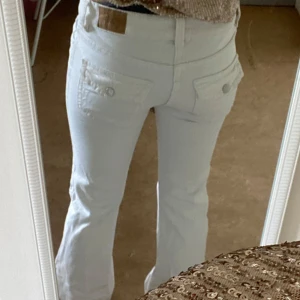 Vita bootcut jeans med fickdetaljer - Säljer ett par vita jeans med bootcut-modell och snygga fickor med knappar bak. Byxorna har normal passform och klassisk femficksdesign. Perfekta för dig som vill ha en fräsch och stilren look.