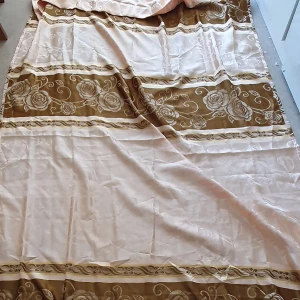 Gardin  - Säljer en stor vanlig gardin i beige och brunt med vackert blommönster. Gardinens kanter har en fin fransdetalj som ger en extra touch av stil. Längd: 248 cm och Bredd: 141cm. (Det är en gardin men vet inte vilken slags men den är inte så tunn)