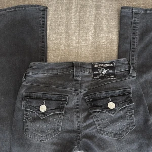 Grå bootcut jeans från True Religion W23 BECCA - Snygga grå jeans från True Religion med bootcut passform och klassiska detaljer på bakfickorna. Jeansen har låg/mid midja, silverfärgade knappar och är tillverkade i mjukt denimtyg.  Är själv 162 och dom passar perfekt i längden men går nog för dom som är 160-165 typ. Säljer då dom inte kommer till användning men har använts få tals gånger. Pris kan diskuteras!☺️