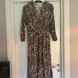 Zebramönstrad långklänning från Pure - Snygg långklänning från Pure med zebramönster i svart och beige. Klänningen har v-ringning och långa ärmar.💕