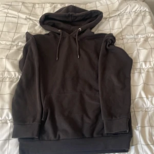 Svart hoodie från Pier One - En klassisk svart hoodie från Pier One med huva och snörning. Tröjan har en stor ficka framtill och är tillverkad i mjuk bomullsmix. Perfekt för chill dagar eller när du vill ha en enkel och stilren look.