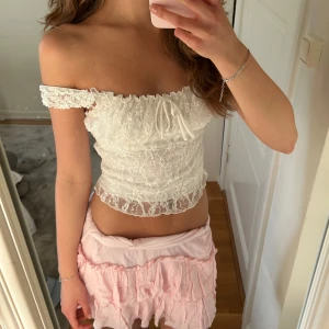 Vit spetsig topp med snörning - Supersöt vit topp i spets och söt snörning framtill. Tunn och luftig, med detaljerad spets över hela toppen och stretchig passform som sitter snyggt på kroppen. 