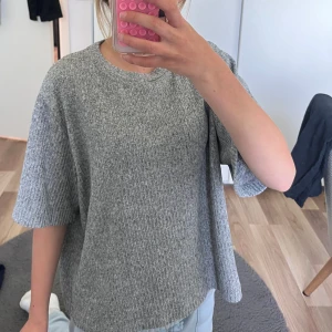 Grå ribbad stickad tröja Lager  157 S - Grå ribbad stickad tröja från Lager 157 i storlek S. Oversized passform med korta ärmar och rund halsringning. Perfekt för lager-på-lager och chill dagar. Mjuk och skön känsla tack vare det stickade materialet.