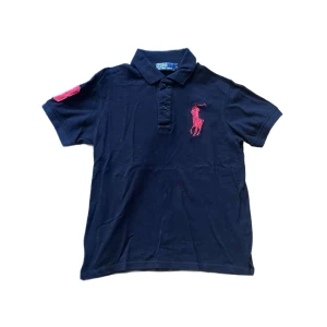 Ralph Lauren piké  - Snygg  pikétröja från Ralph Lauren med klassisk krage och knäppning framtill. Stor röd broderad logga på bröstet och röd detalj på ärmen. Tillverkad i bomull och har korta ärmar. Perfekt för en stilren och sportig look. Observera pikens färg på bild 2-5 istället för 1 . Jag skickar ej bild när jag bär plaggen och jag vet ej vilken längd och vikt de passar då jag inte prövar kläderna jag säljer 😃