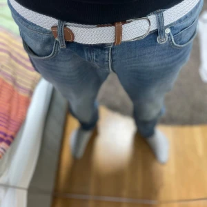 Vitt flätat bälte  - Snyggt vitt flätat bälte med bruna skinn-detaljer vid spännet. Perfekt accessoar för att lyfta din outfit och funkar grymt till jeans. Bältet har en stilren look och passar dig som gillar en clean och modern stil. Helt nytt!