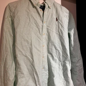 RALPH LAUREN skjorta grön - Snygg slim fit skjorta från Ralph Lauren i grönt och vitt randigt mönster. Klassisk button down-krage, broderad logga på bröstet och knäppning framtill. Tillverkad i mjuk bomull och med långa ärmar. Perfekt för en clean och fräsch stil.